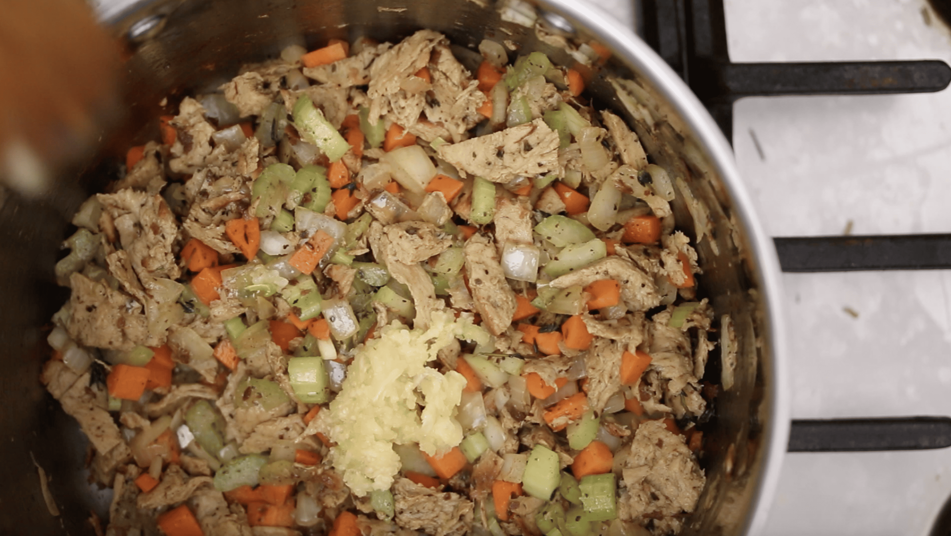 minced garlic being added to a pot of soup