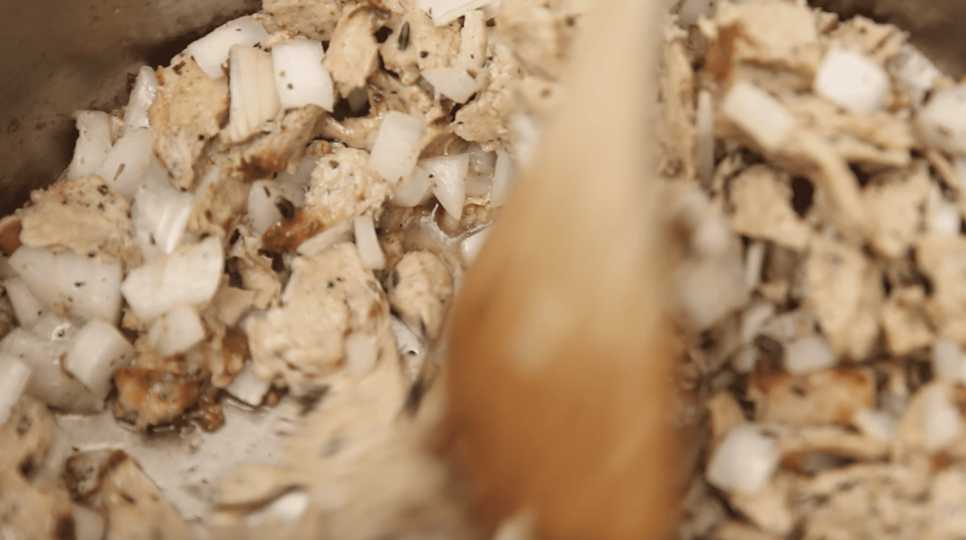wooden spoon stirring onion and chicken in a pot