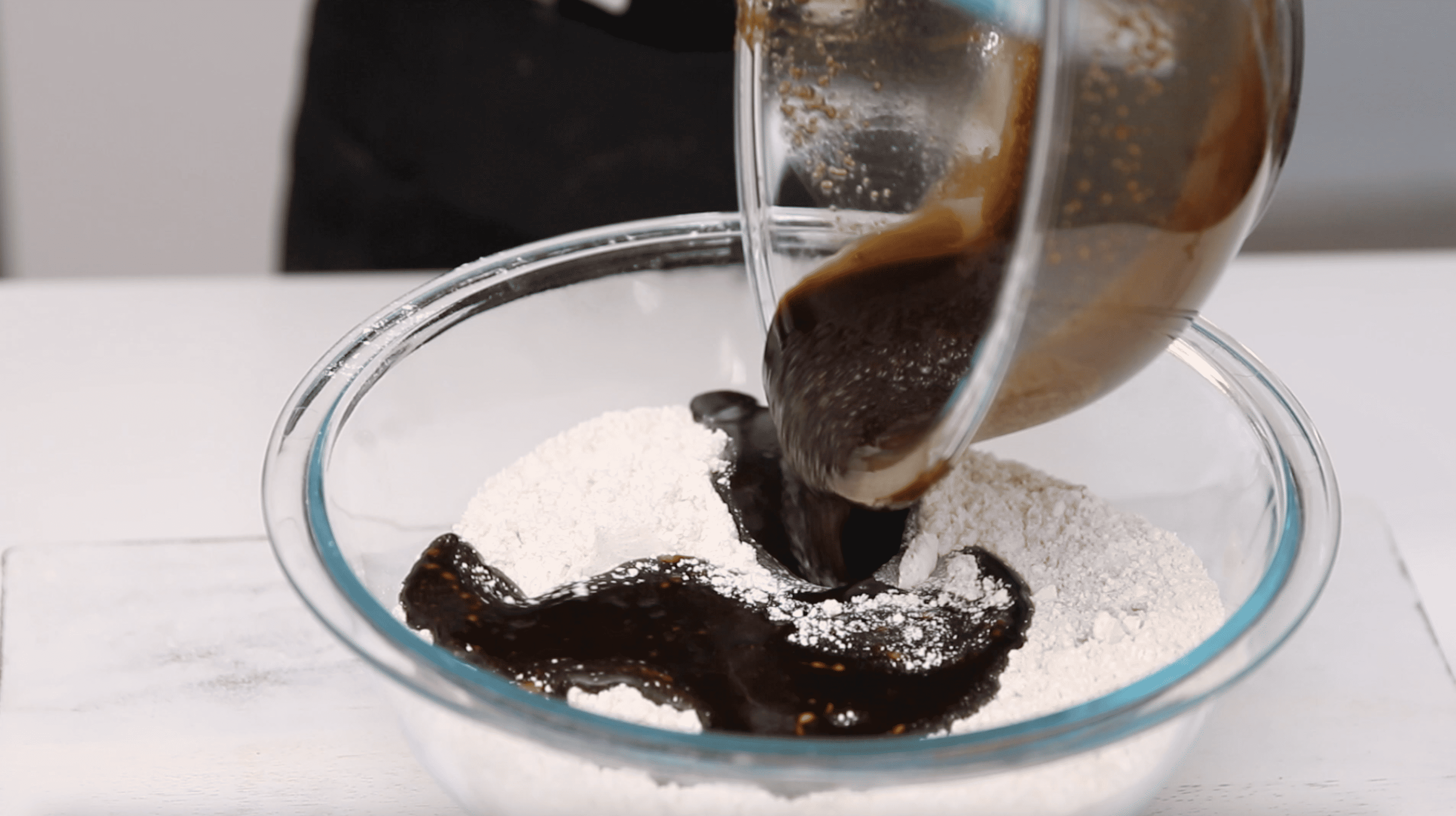 wet ingredients being poured into a mixing bowl of flour