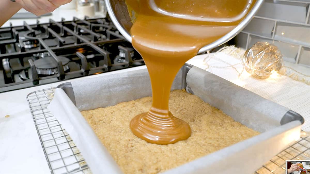 caramel being poured onto a shortbread crust in a baking pan