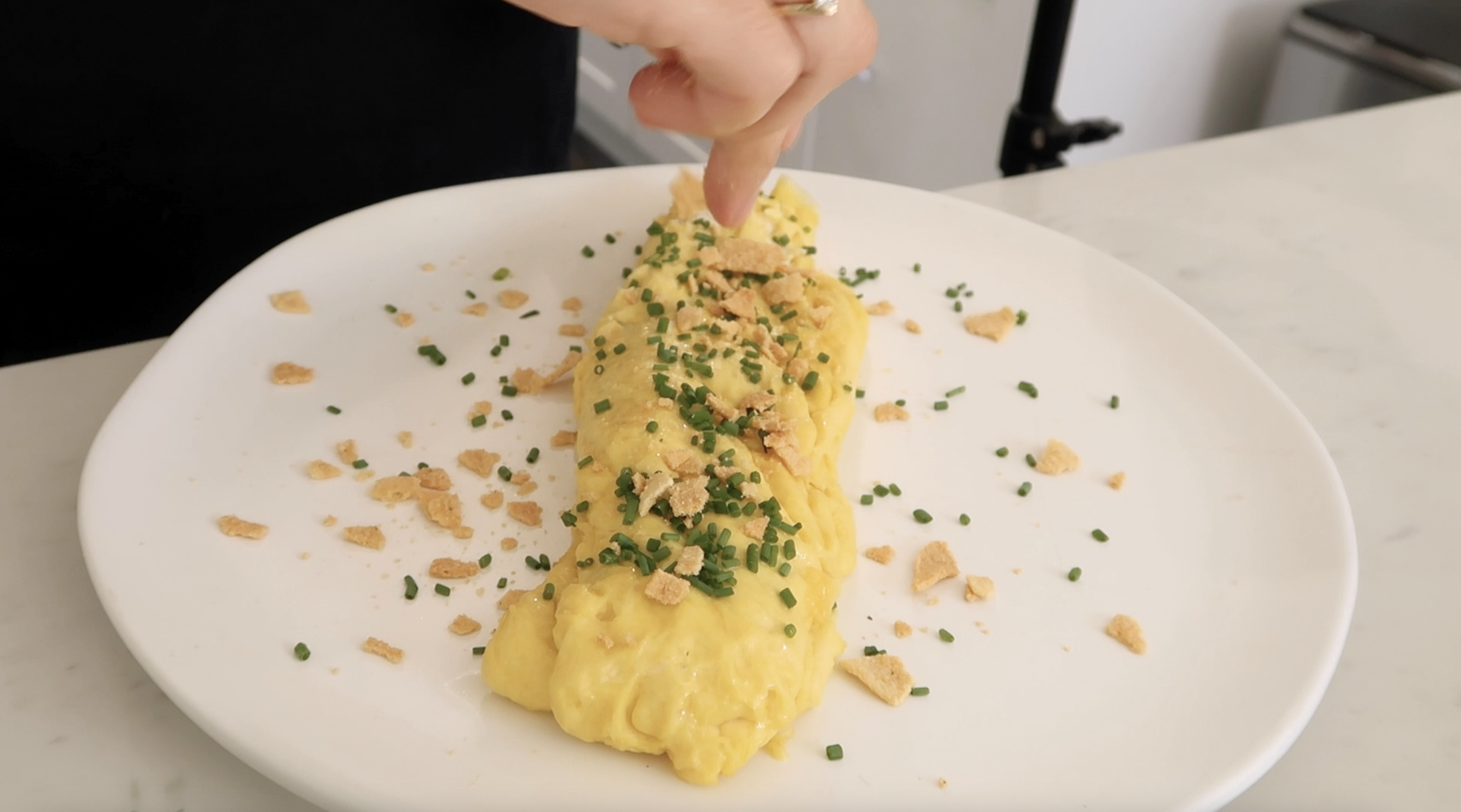 hand garnishing omelette with chips and chives