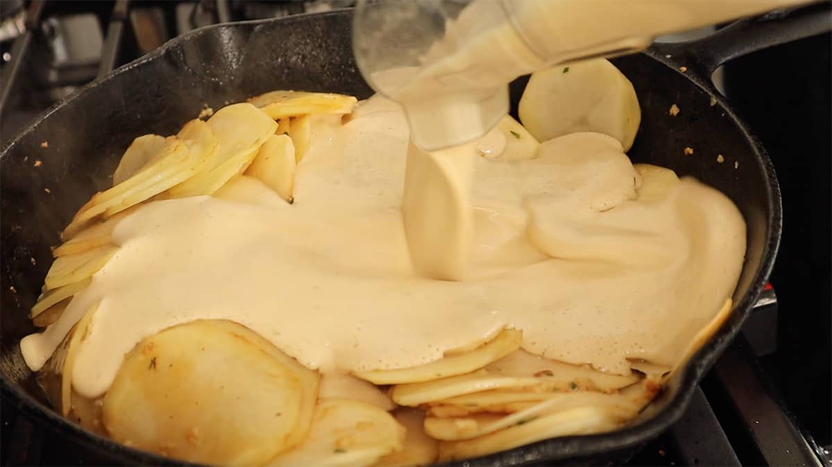 a skillet with sliced potatoes in it and cream being added