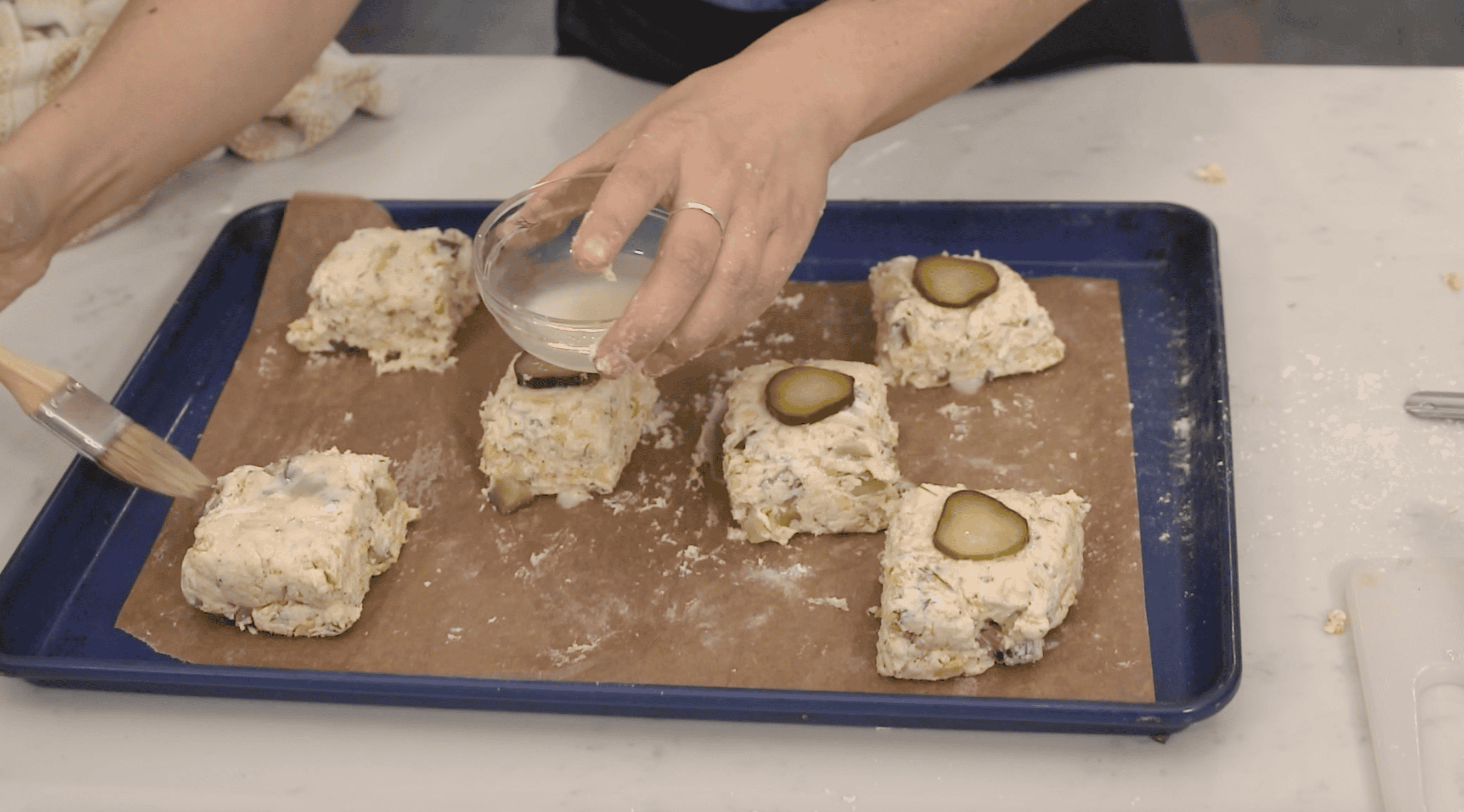 brushing biscuits with vegan egg wash and topping with a pickle slice