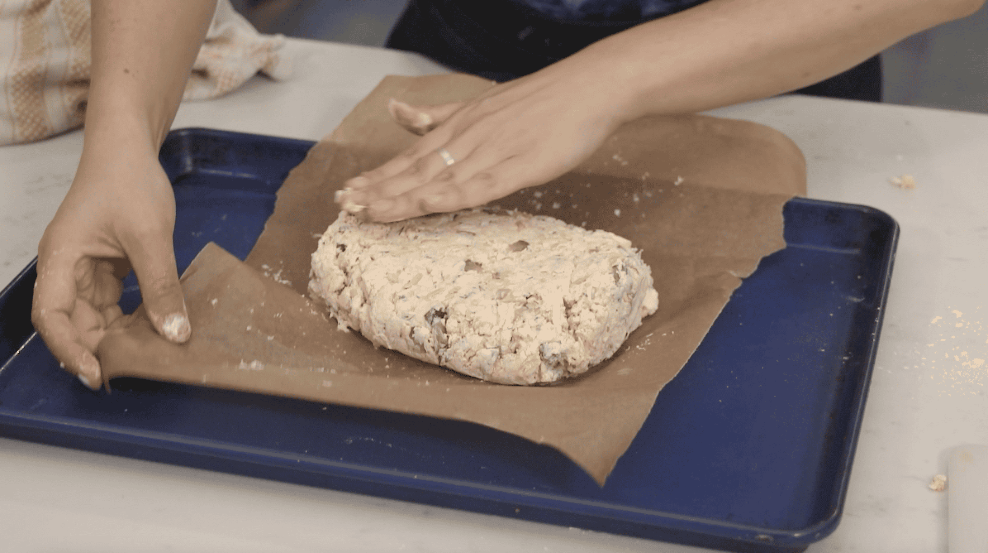 hands flattening biscuit dough on a parchment lined baking sheet