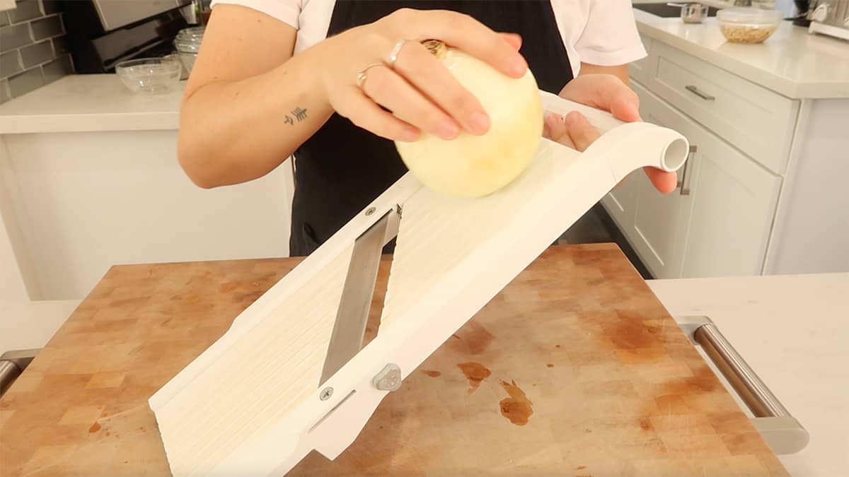 hands are holding onion and slicing it on a mandolin