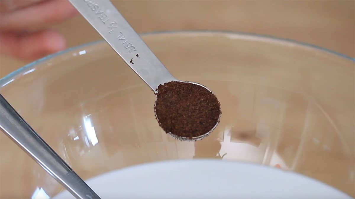 a teaspoon of vanilla powder over a mixing bowl of coconut milk
