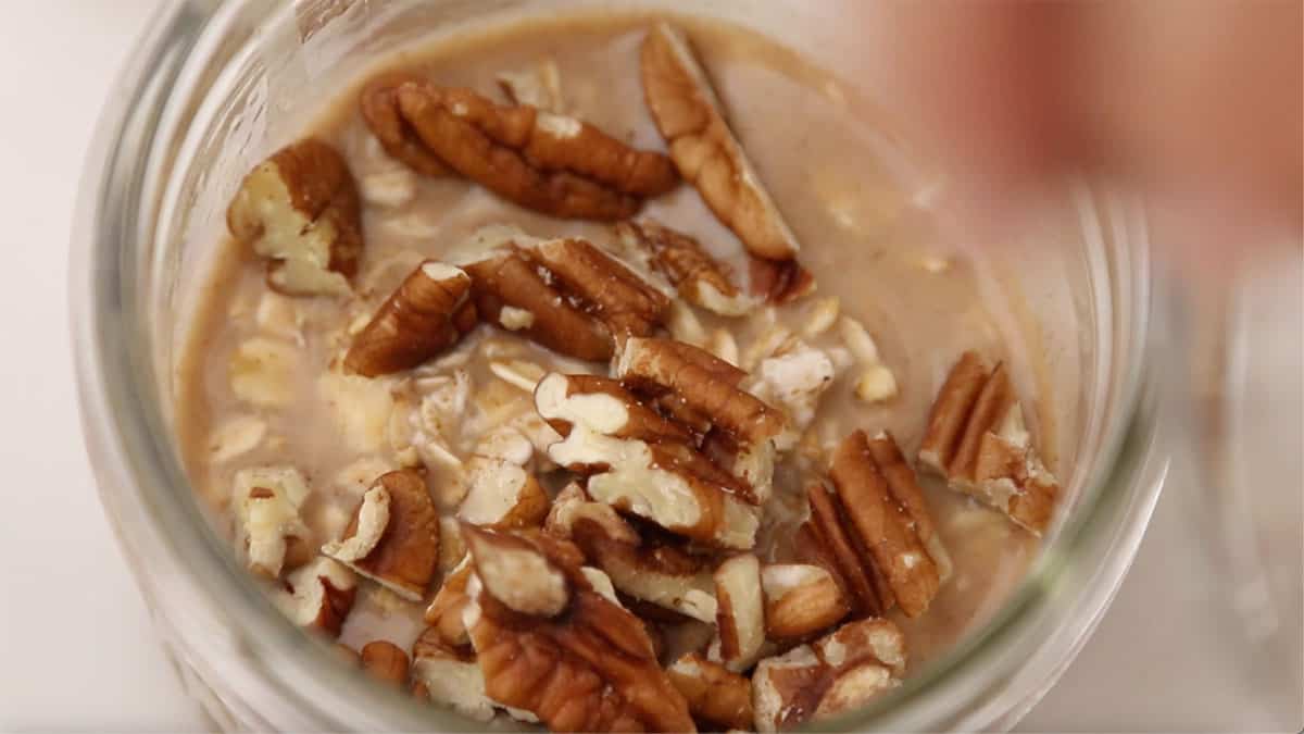 jar of overnight oats with pecans being added on top