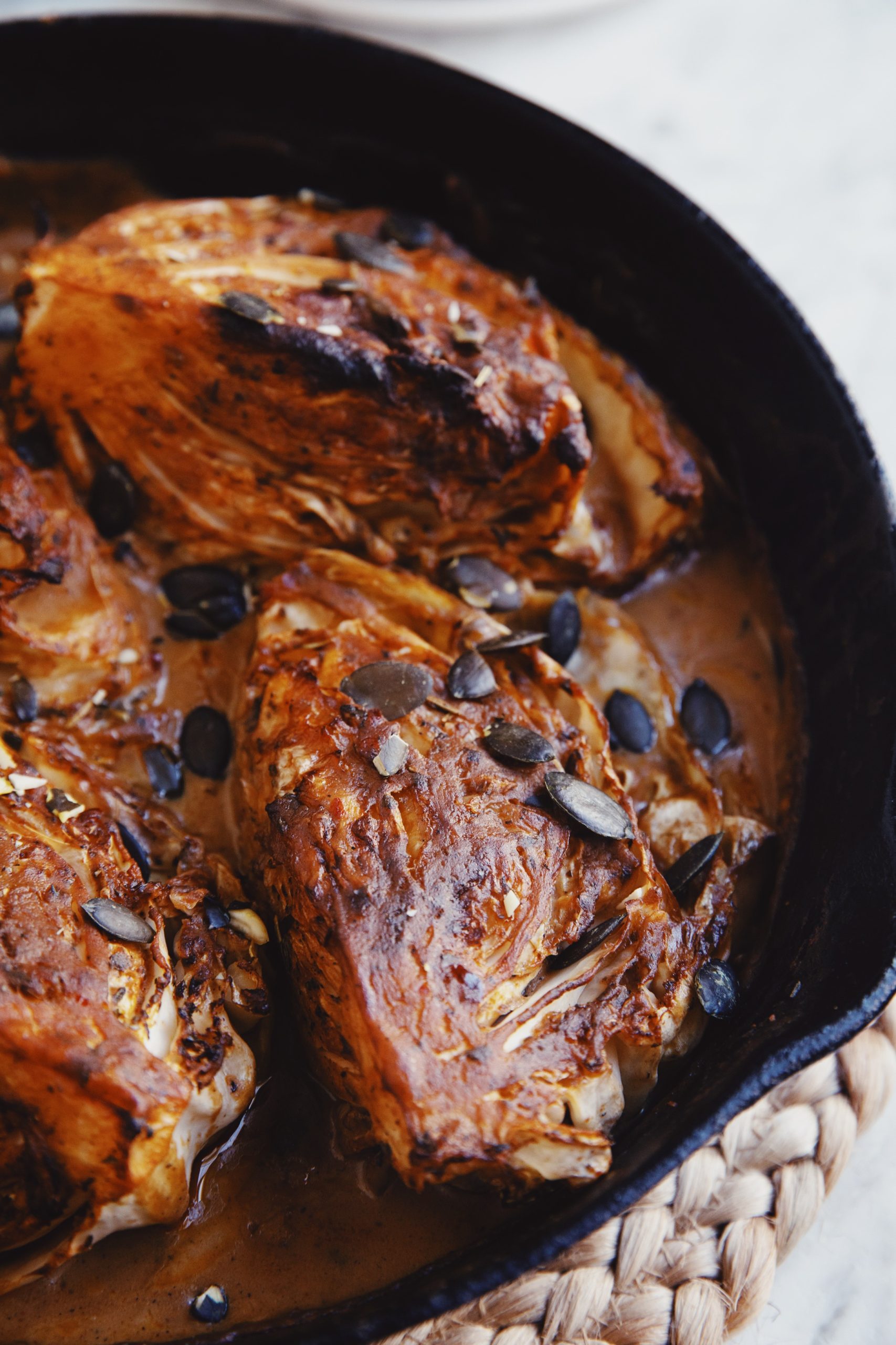 vegan braised cabbage in a cast iron pan with charred edges and savoury braising liquid
